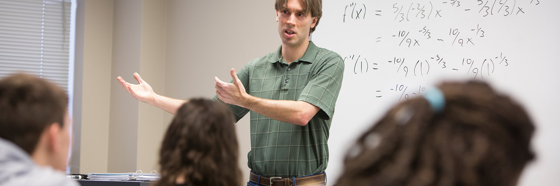An instructor lectures in front of a whiteboard filled with equations.